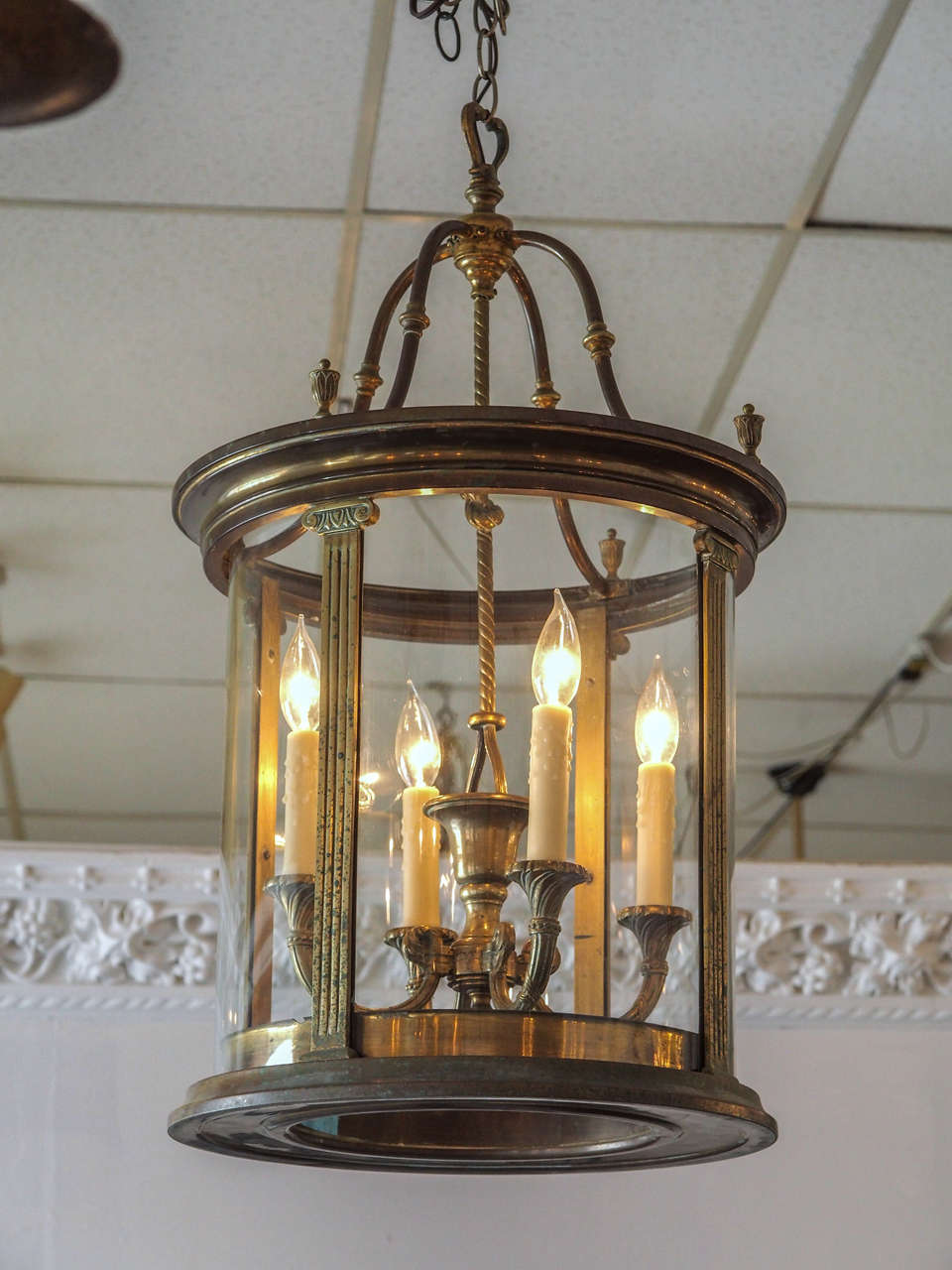 French, circa 1930s cylindrical paneled glass and brass lantern, early 20th century. Brass ionic columns separate the panels. Brass finials are placed above each column on the upper rim. The interior, fitted with a pendant four-light chandelier