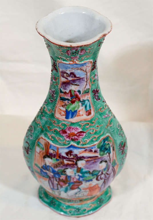 A pair of flattened baluster shape Chinese export vases with a green dimpled skin ground. They have shaped panels front and back. Each vase is painted in Famille Rose enamels depicting Chinese Mandarin figures in the garden of their home.  The neck