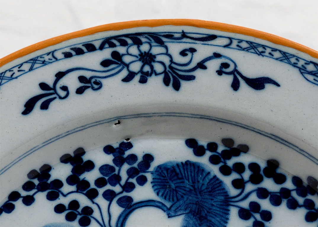Provenance: From the collection of Katherine Mellon
A pair of Dutch Delft Blue and White chargers showing a garden scene. The edges are painted orange. On the reverse is the mark of 