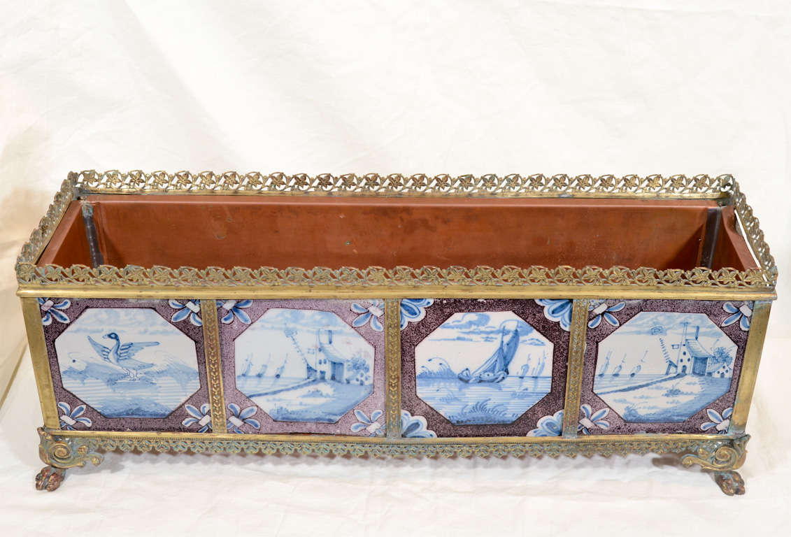 Provenance: From the collection of Katherine Mellon
A 20th century brass jardiniere lined with copper and decorated with 10 18th century London Delft tiles showing Blue and White waterside scenes of sailing ships and castles within powdered