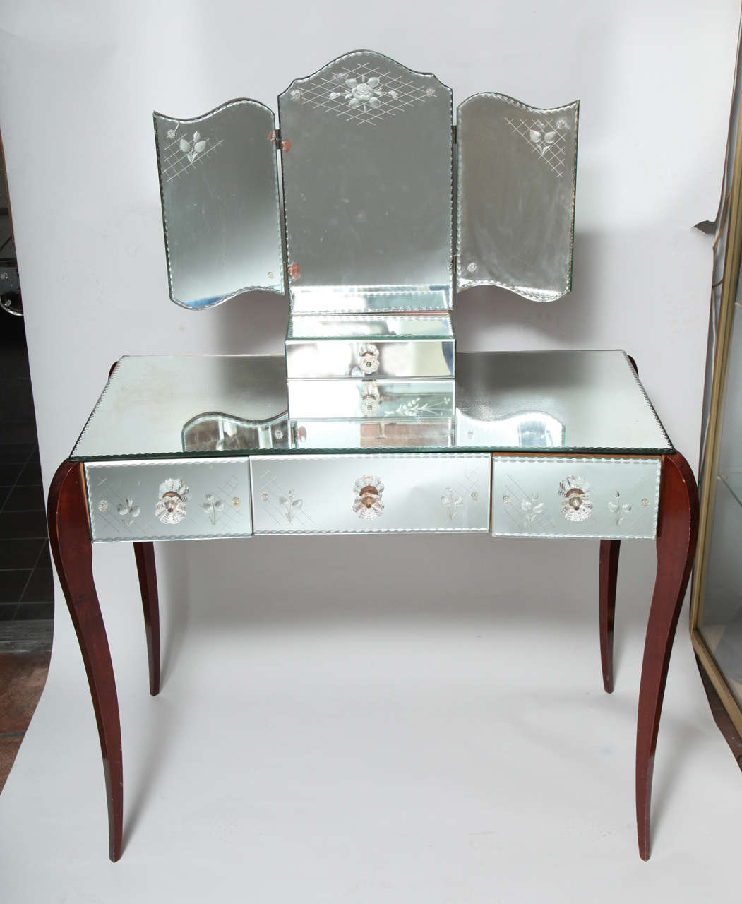 A stunning vanity with delicate french floral etching on pie crust edged mirrored panels and glass handles. A folding matching mirror sits on top a jewelry box. The cabriole legs are sycamore