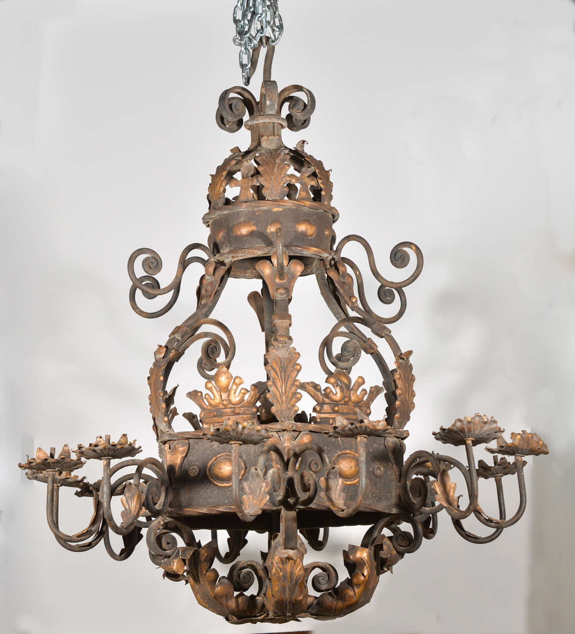 This French patinated metal and iron chandelier has curving, flowing lines of gilded c and s-scrolls with
acanthus leaf and crown motifs .  It has twelve arms emanating from a thick, six sided, partially gilded, decorated panel, with bobeches