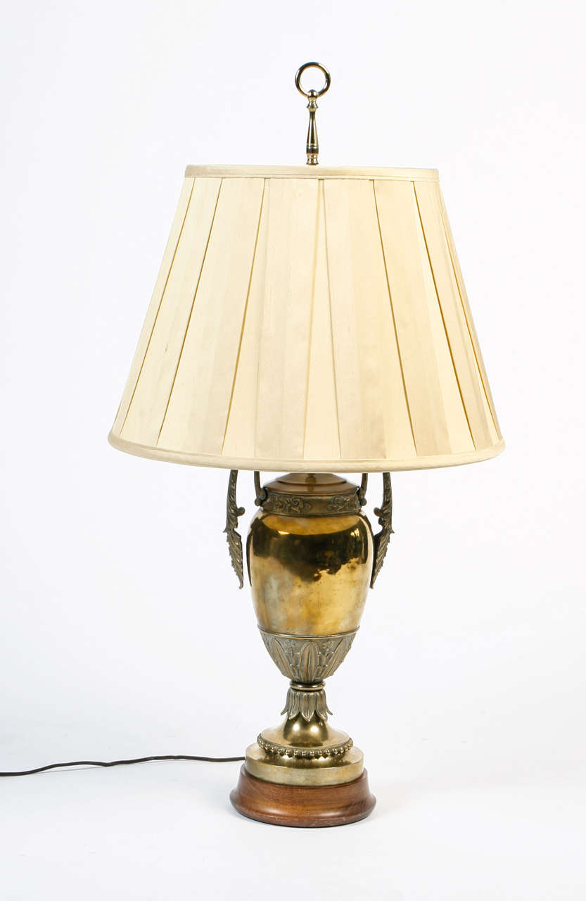 Brass lamp with handles positioned on wood base. Incised bronze with leaves and flowers. Pleated silk shade. Electrified.