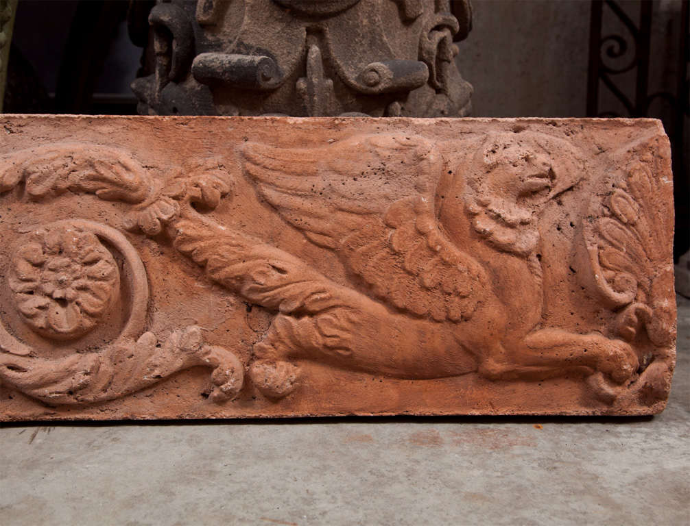 In spite of the lead photo here which incorrectly depicts the same plaque twice, this is a wonderful pair of opposing wall plaques, fabricated from a rich terra-cotta-colored cast stone.  Two opposing winged griffins are flanked by