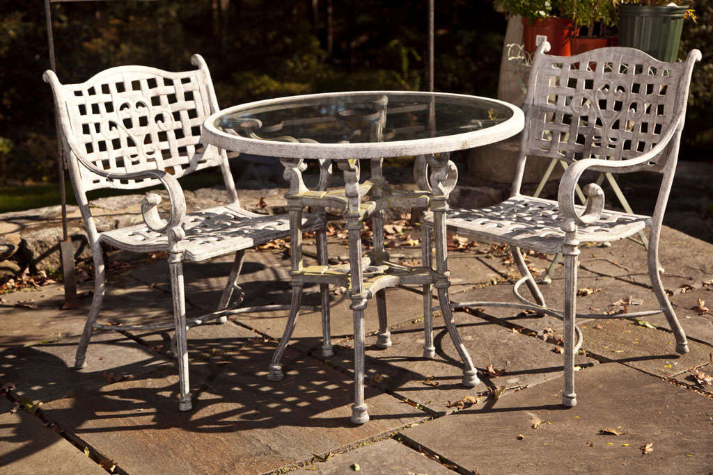 VERY DETAILED CAST METAL OUTDOOR OR INDOOR TABLE AND TWO CHAIRS PAINTED ANTIQUED OFF WHITE FINISH- TABLE HAS SET IN CLEAR GLASS TOP- CHAIRS21 1/2W X 23