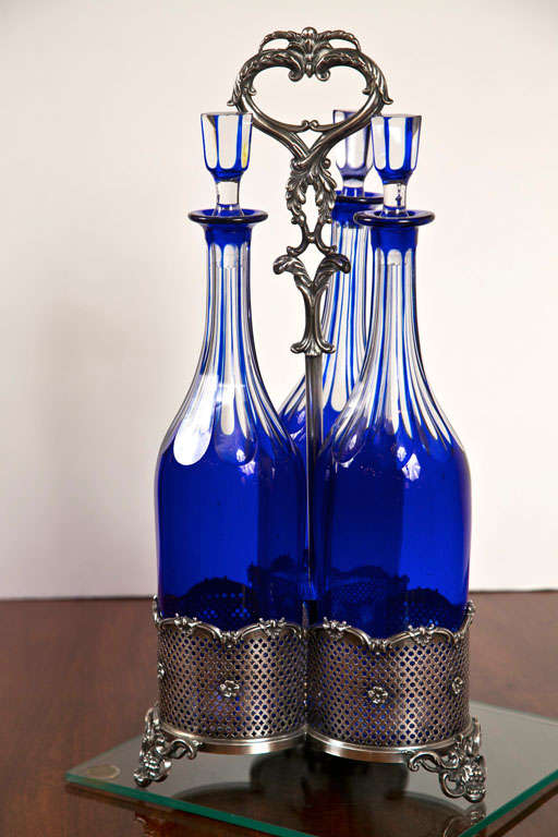 The stunning cobalt blue crystal of these decanters is offset handsomely by the silver trivet caddy that holsters them. Rococo influence is seen in the details of the caddy, not the least of which are the grapes and leaves adoring the feet.