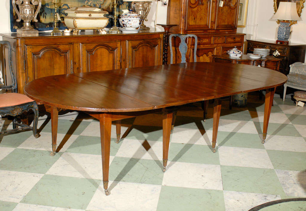 A Directoire French extending walnut dining table with 3 leaves, tapered legs and brass castors.  THE TABLE HAS 2 EXTRA PINE LEAVES THAT EXTEND THE TABLE TO 151