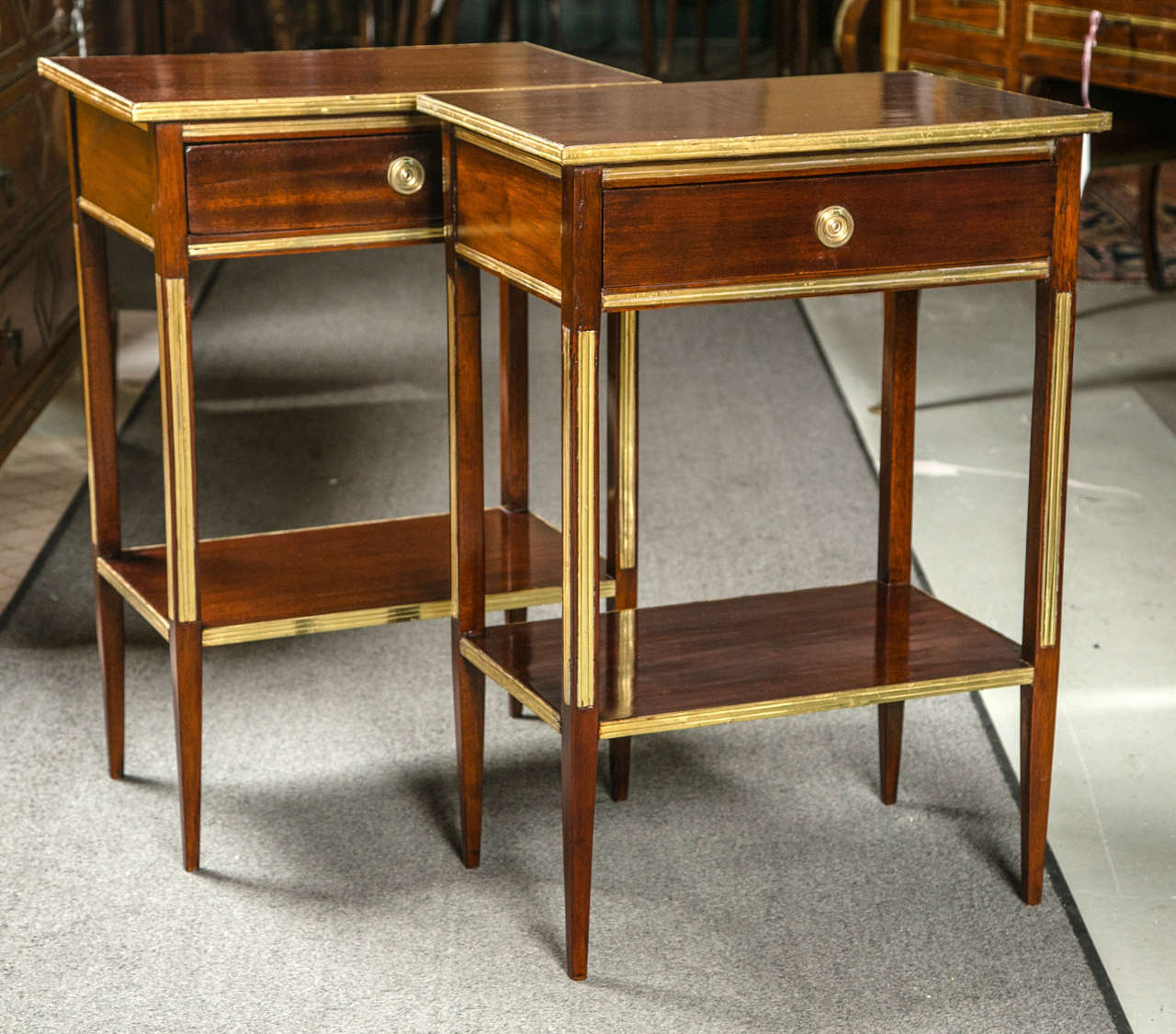 A wonderful pair of bronze mounted nightstands or end tables. The narrow tapering legs leading to a lower shelf used as an undercarriage supporting the continuing legs with bronze fluted mounts on front and sides leading to a single bronze framed