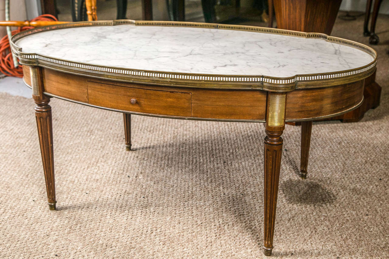 Louis XVI style marble-top low table or coffee table by Maison Jansen. This fabulous low table with Carrara white marble top with grey veining surrounded by a bronze gallery shows bronze cookie corner mounts at each top corner of all four fluted