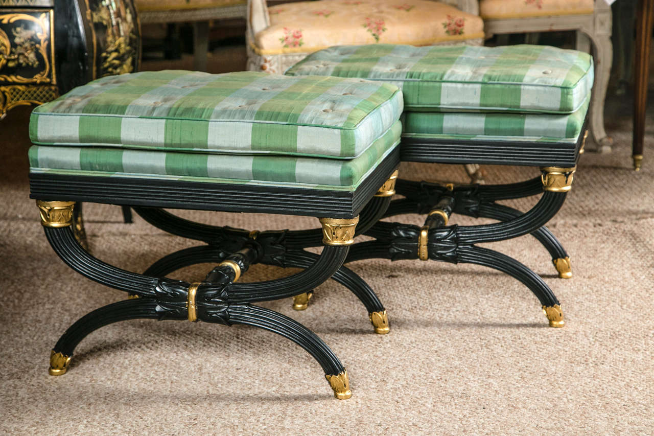 Ebonized with gilt gold accents applied to this finely carved and detailed X form bench depicting the flavor of the Hollywood Regency Era. The gilt caped feet flowing into a reef carved X form base terminating in gilt gold capitals.