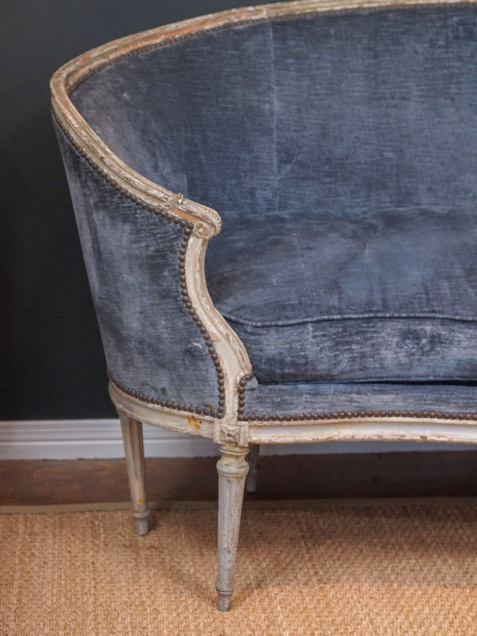 19th century french sofa with surround arms, whitewashed and carved frame with central bow motif and fluted supporting legs.  Upholstery is an old, beautiful blue grey and is framed with brass studs.