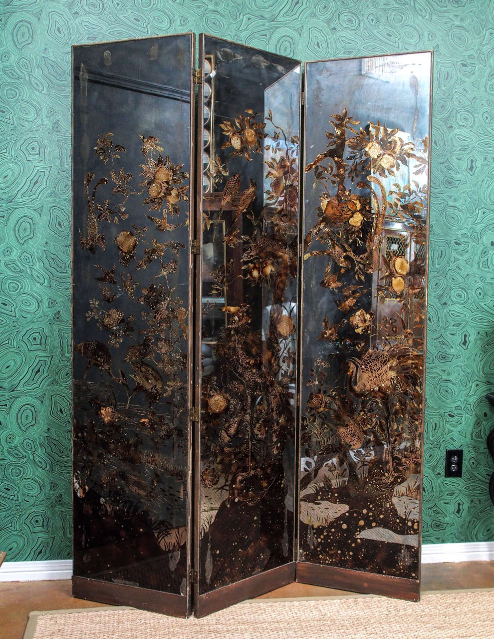 Three-panel screen with antiqued mirror front and back. Reverse-painted in traditional Verre Églomisé style with flora and fauna scenery. Backside features mirror from top to bottom, so screen can be freestanding in any part of a room.