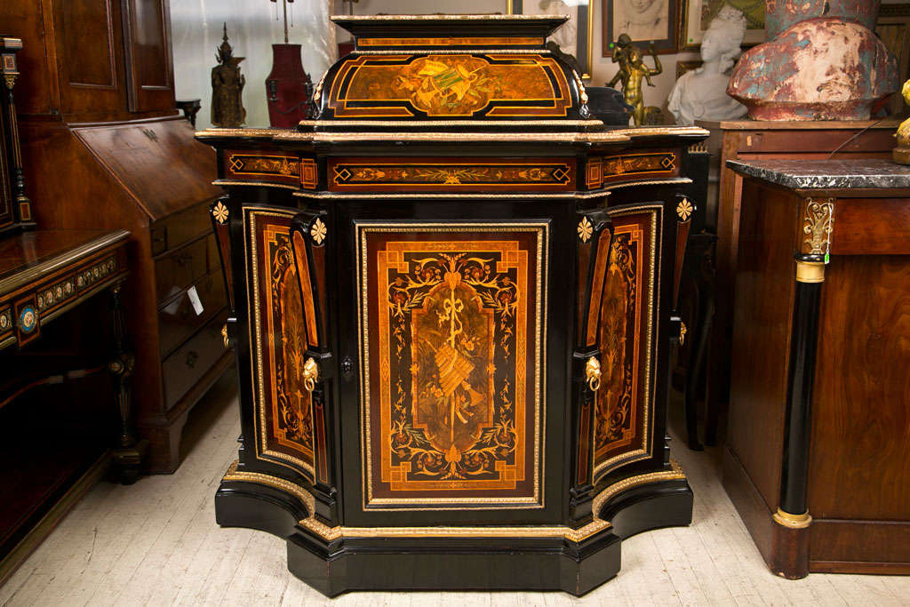 DRAMATIC CREDENZA  INLAID WITH  MUSICAL INSTRUMENTS, FLOWERS AND VINES. EBONIZED WOOD, GILT  BRONZE EDGING. SPRING ACTION CENTRAL DRAWER ABOVE A SINGLE DOOR CABINET. GILT BRONZE  LION HEAD MASKS. PROBABLY MADE FOR SHEET MUSIC.
PLEASE FEEL FREE TO