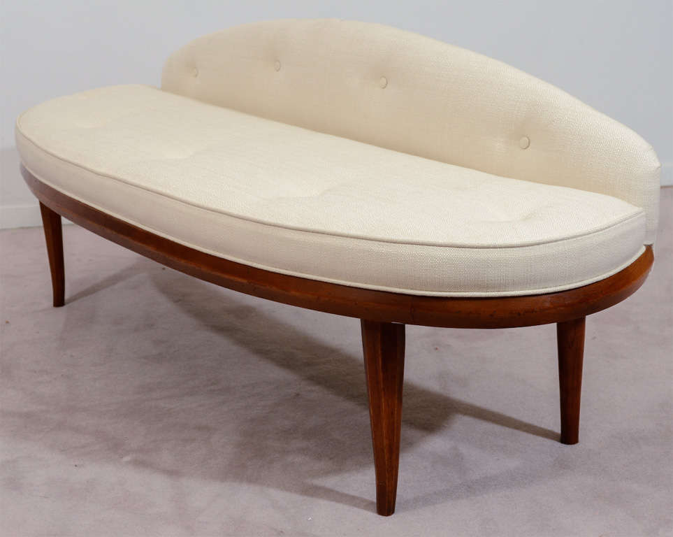 A vintage wood frame bench with newly reupholstered ivory colored tufted cushions.