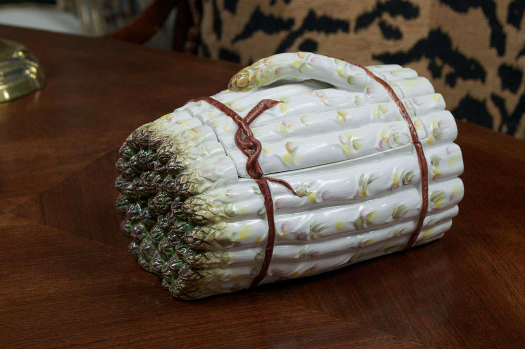 The bundle-form dish of horizontal asparagus spears with fitted single-handle lid opens to a craquelure interior; hand-painted ‘Italy’ on the underside.