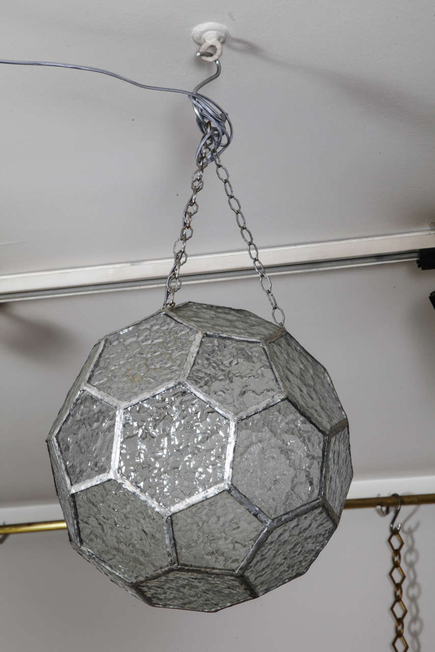 Round pendant with hexagonal translucid glass faces mantained by a metallic fishnet and suspended by a chain