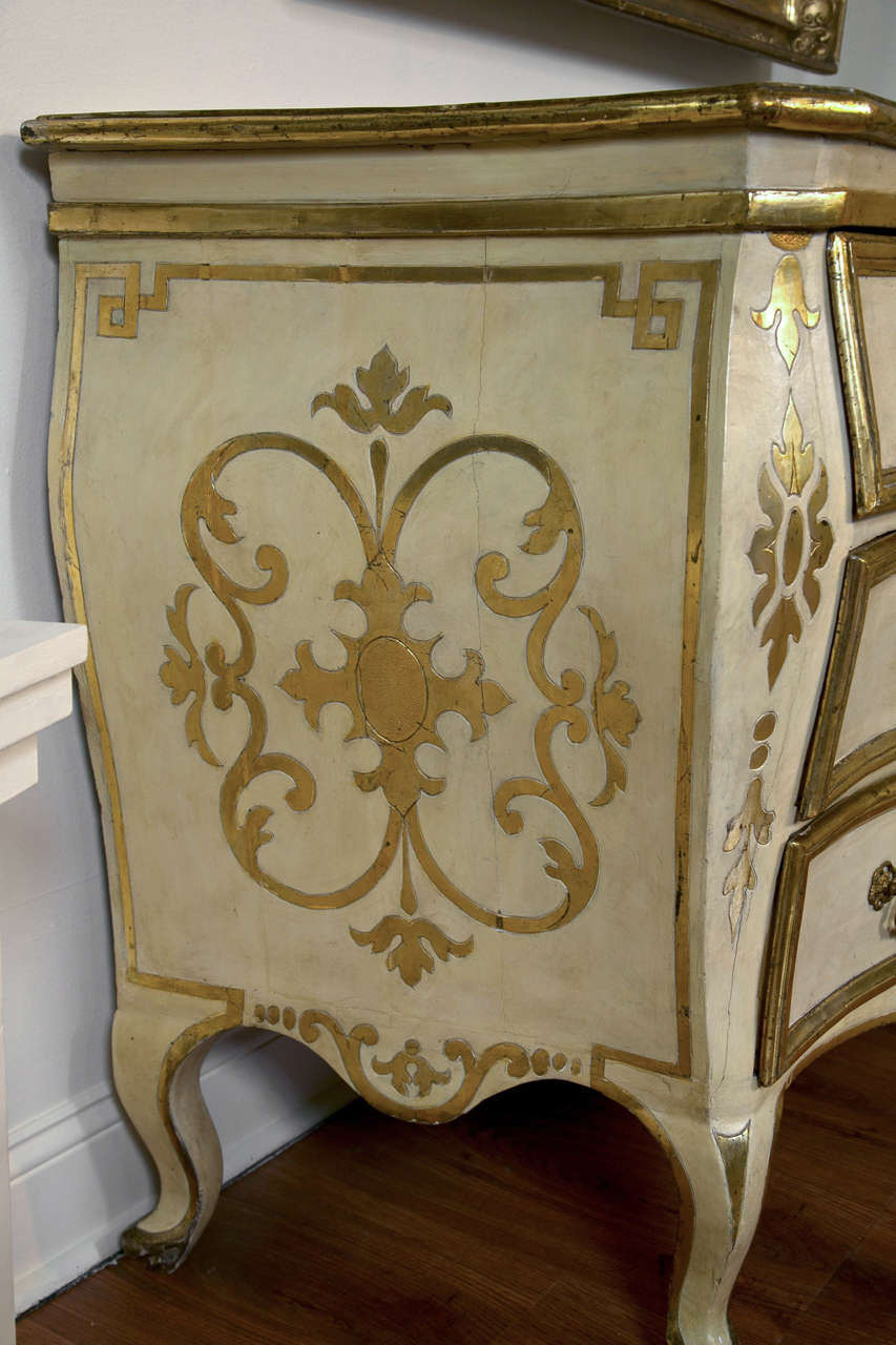 An exceptional pair of Italian rococo bombe cream painted and parcel gilt commodes retaining their original redecorated faux marble top and shaped cabriole feet. The front and sides similarly decorated with gilt arabesque designs, refreshed paint,