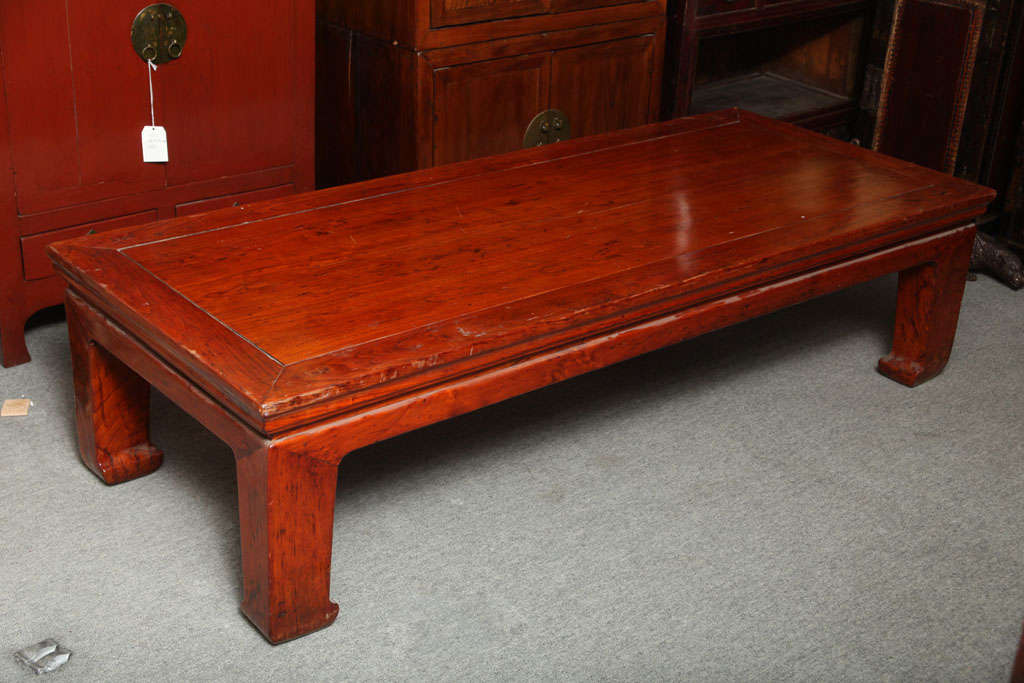 A red lacquered Elmwood Chinese bed / coffee table from the 1800s. The red lacquer displays a soft patina, typical of traditional Chinese lacquer art.  This table features a clean top with a central panel and a wide trim surround.  The top rests on