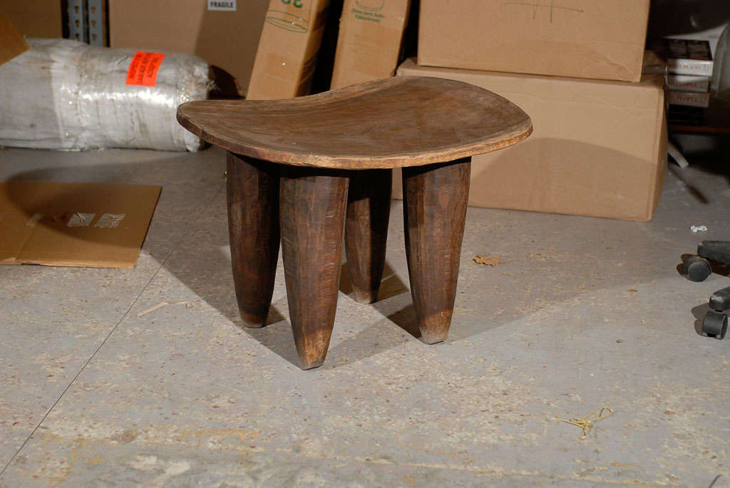 Rustic African wooden stool with hand carved tapering legs and a curved seat.