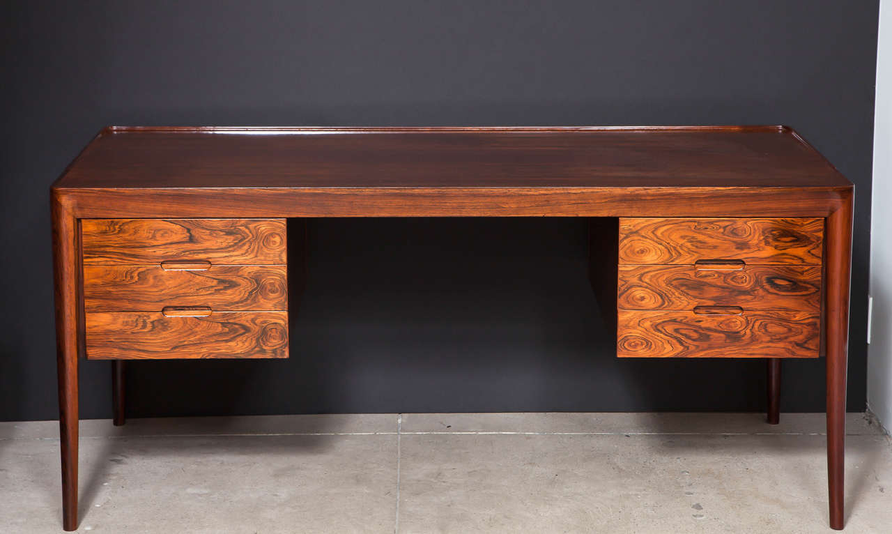 A Danish writing table designed by Severin Hansen and produced by Haslev Møbelsnedkeri, Circa 1960s, well figured rosewood, of floating form with three drawers each side, raised on circular tapered legs.