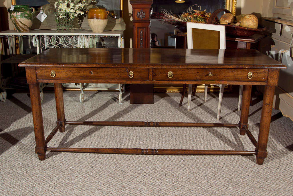 A French oak farm table, circa 1930s, the rectangular top over a frieze fitted with two long narrow drawers with brass patera loop pulls, raised on circular legs joint by box stretcher, ending in block feet.