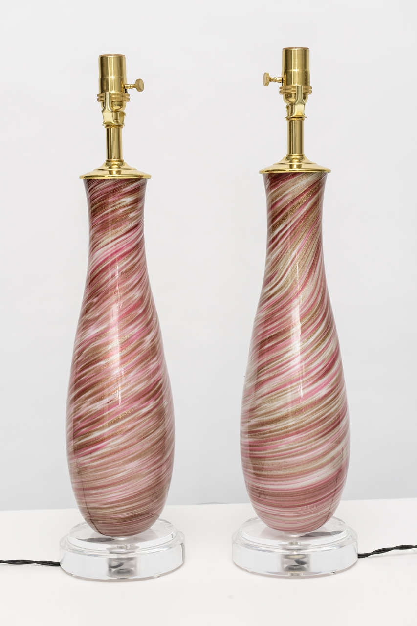 Pair of vintage Murano glass lamps with swirling pattern of pink, red, and gold with Lucite bases and brass hardware.