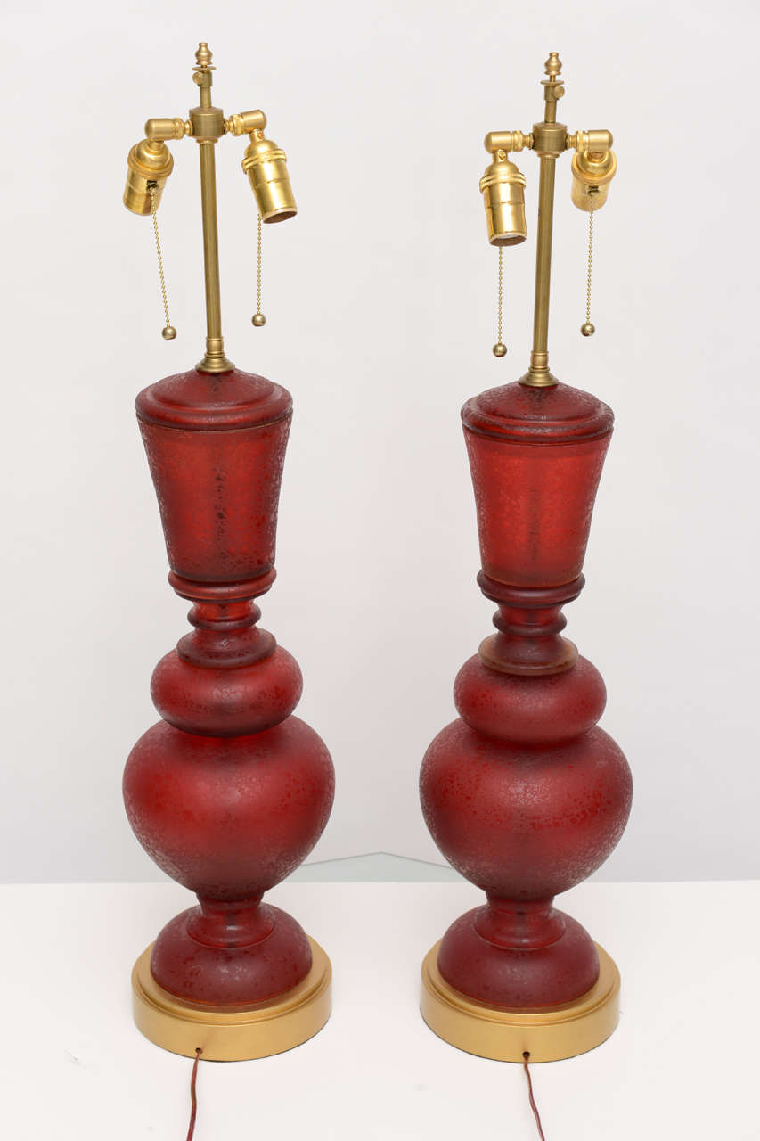 One pair of sumptuous red satin scavo Murano glass lamps with smooth gilt plaster bases. Brass fixtures, finials, and pulls and transparent red cords. Original wiring.