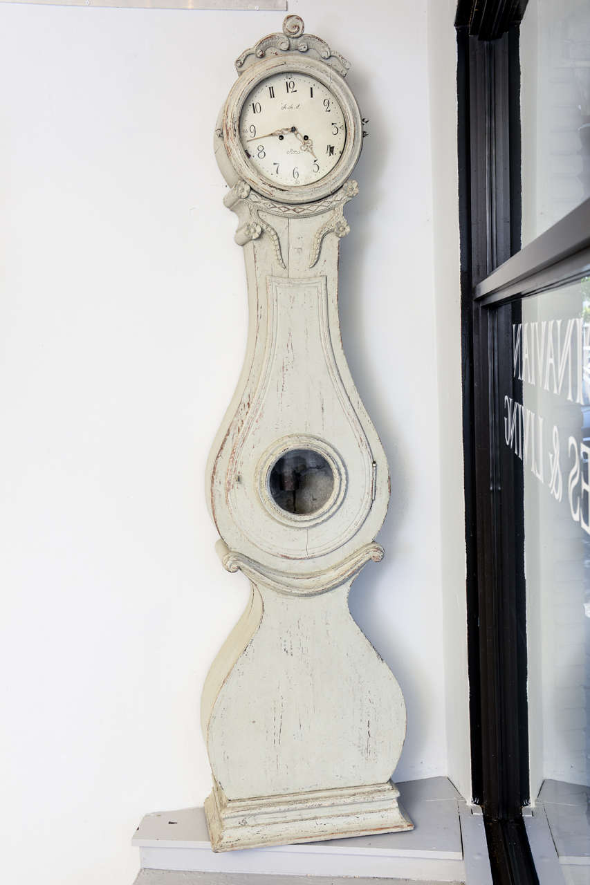 A Swedish Bridal Clock from Jamtland with elaborated carved floral decoration & carved crown on the bonnet, early 19th century. Light grayish/white paint.The clock is in a working condition.
