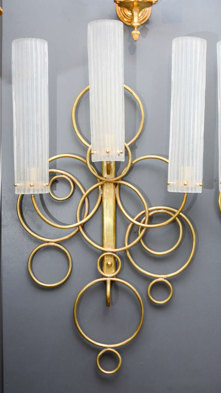 Nice set of four tall wall sconces made of brass and white textured glass.
Each sconce has several brass circles which gives a light overall aspect.