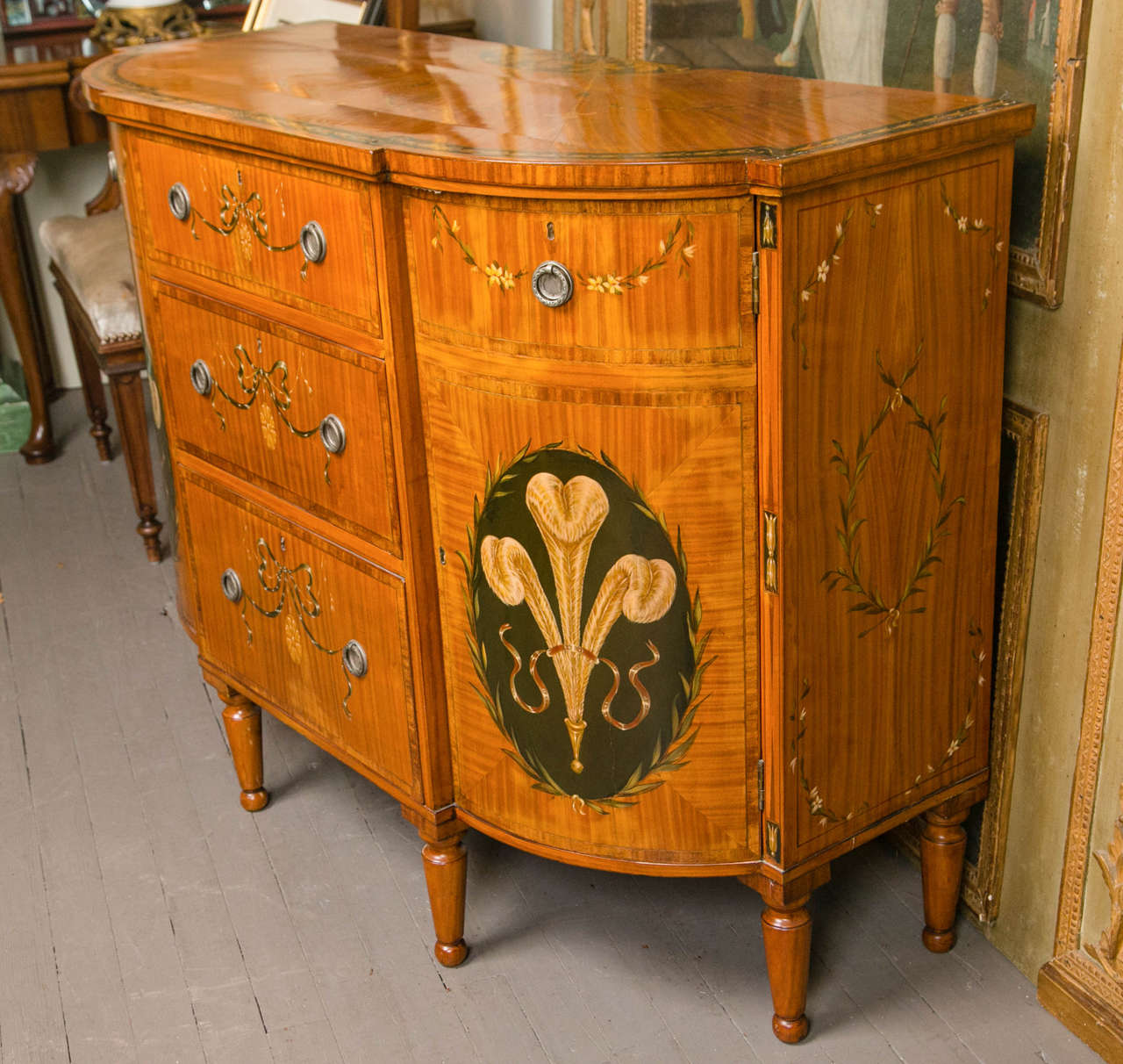 Three central drawers flanked by swing out, curved door cabinets.
Of Satinwood or Kingwood,  with hand painted decoration including Prince of  Wales  feathers, swags, bows, small flowers. Cross banded   drawer and cabinet fronts.