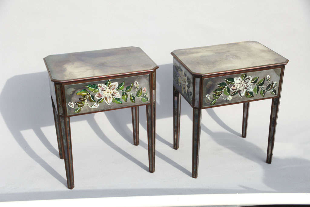 Pair of end tables, each having rectangular smoked mirrored top with canted corners, with single frieze drawer, reverse painted floral images on all sides of apron, raised on square tapering legs.