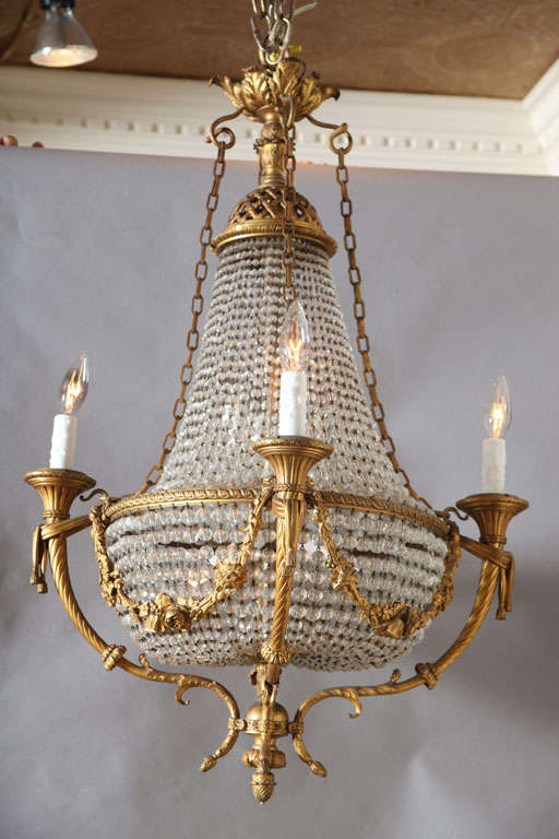 Exquisite Empire chandelier, having a frame of finely chased gilt bronze, basket shape, draped in beaded crystals; floral swags connect the four external candlearms, four additional lights inside basket.