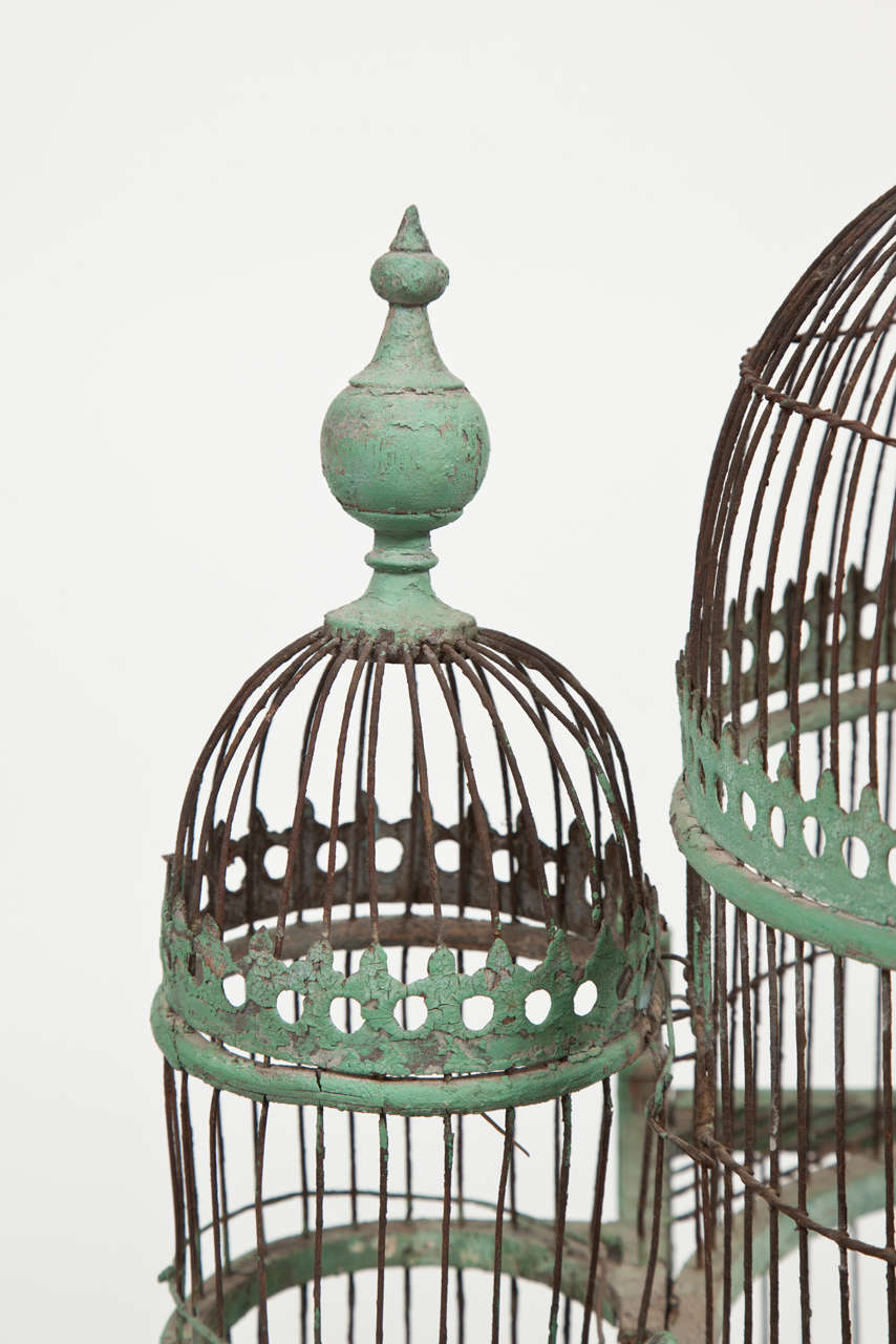 A double-domed large green painted bird-cage with side domes and onion-shaped finials. The arched doors in the main section with fleur-de-lis and with sliding trays below, and feed trays at the sides. Supported on turned feet.

Probably French,