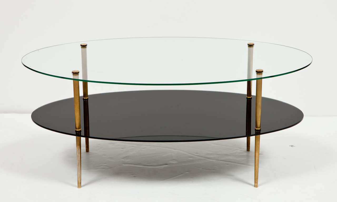 Oval coffee table with glass top over black glass lower tier shelf supported by brass plated reeded legs