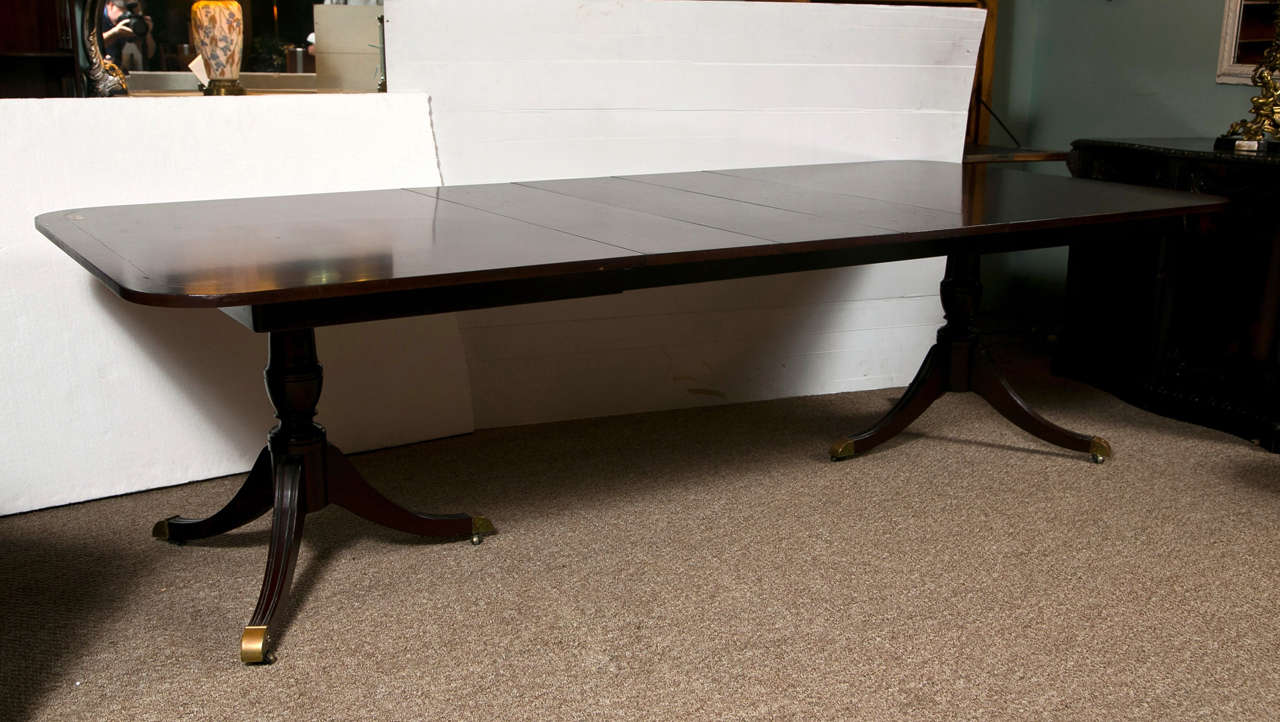 English Regency style dark mahogany banded dining table on double pedestal. Custom Quality by Kindel Grand Rapids Michigan. Has four leaves. Solid Mahogany has measured  12 inches long by 46 inches wide Recently hand rubbed French polished.