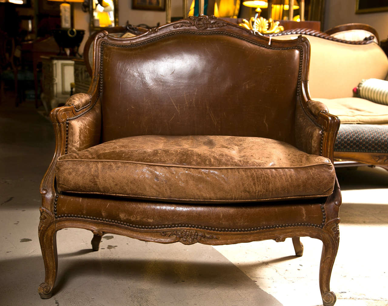 French Provincial style walnut bergere chair, upholstered in distressed brown leather, padded back, downswept arms and cushioned seat, raised on cabriole legs ending in scrolled toes.
