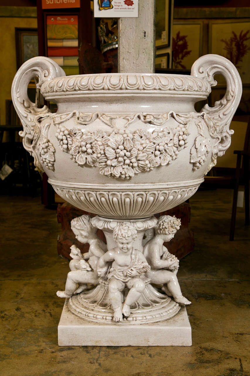 Large pair of Vintage, Classical Style crackled glaze terracotta urns. Monumental handled urns.  Each has four cherub design base with traditional elements.  Embossed swags of vine leaves, acanthus, and grapes with foliage.  Decorated cherubs