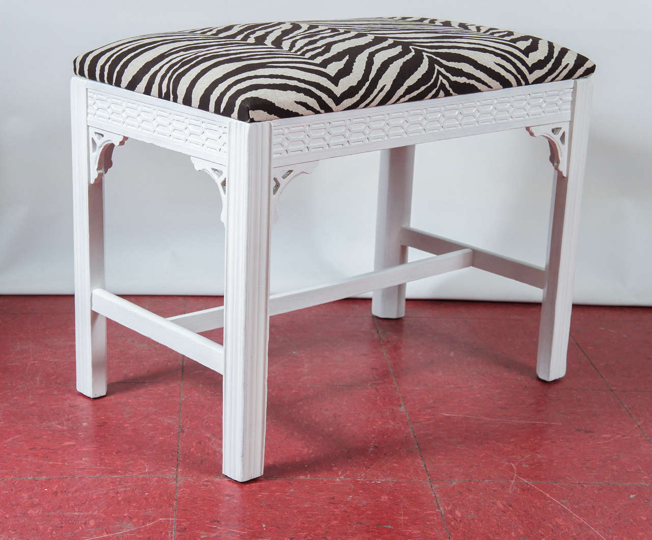White painted bench/ottoman or stool with zebra linen upholstery, carved apron panels, decorative corner brackets and stretchers.