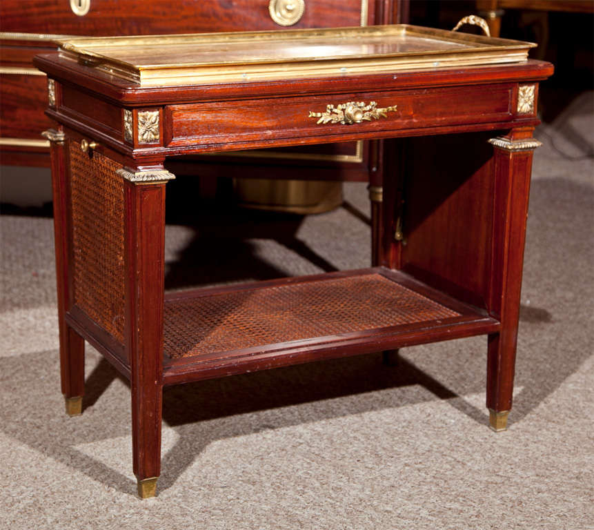 French Louis XVI style mahogany and parcel-gilt serving table, brass tray top that is removable, caned sides and lower tier, raised on brass caps.