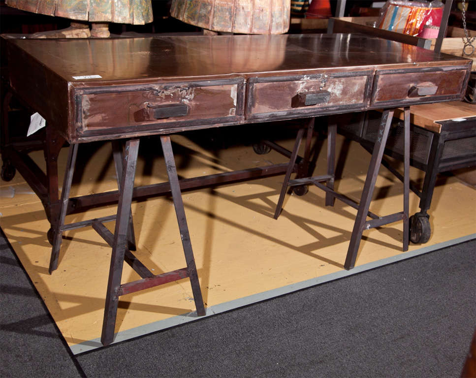 Industrial metal writing desk, rectangular top with three drawers, raised on trestle stands, overall patinated as an intended character. Very attractive.