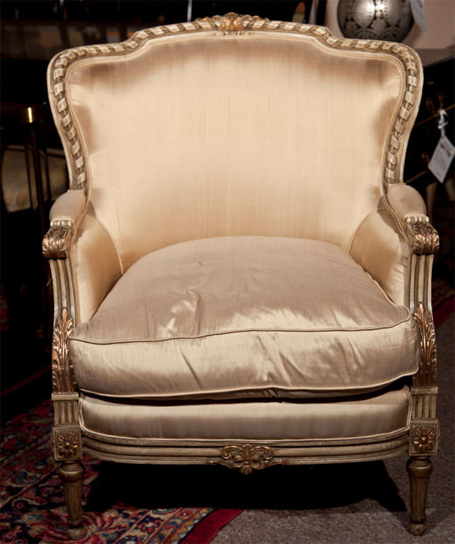 Pair of creme peinte and parcel-gilt French bergere chairs in the taste of Louis XVI, molded back with padded arms and cushioned seat, raised on fluted legs. Upholstered in silk.