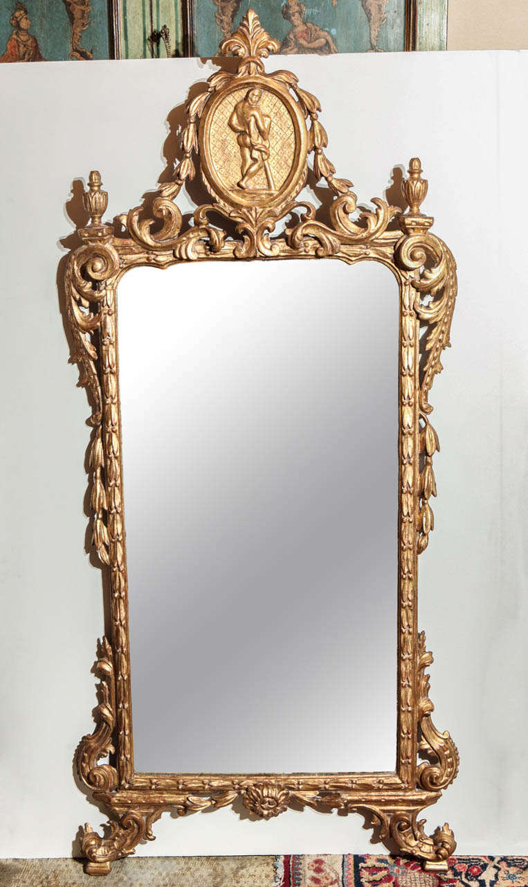 Hand-carved and gilded, pier mirror crowned with a figural, relief medallion embellished with drapery swags. The frame is inset with mercury glass mirror.