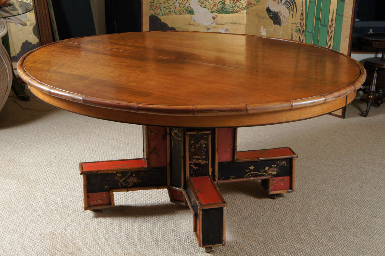 Here is a beautiful custom oval dining table in the style of Jansen. The table has a bamboo surround with two leaves and folding bamboo end legs for support when opened. The base is is in the original hand painted lacquer with some distressing.