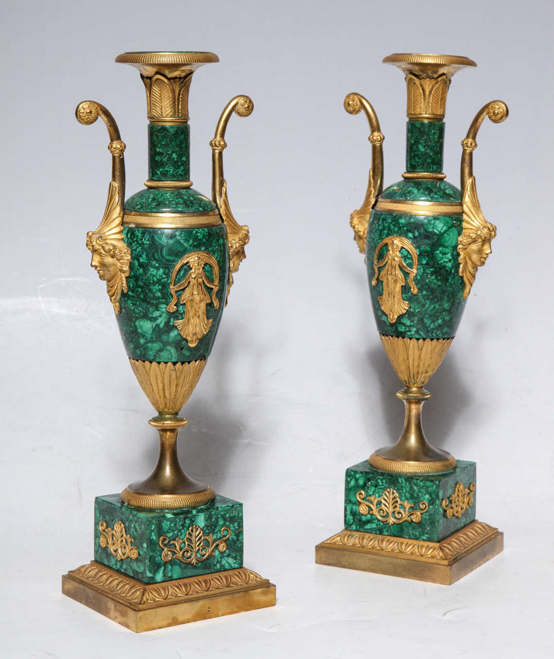 Pair of neoclassical Empire period Russian malachite and dore bronze double handled vases. The vases are decorated with matte and burnished two toned dore bronze, beautifully chased dancing female figures and intricately carved female face masks on