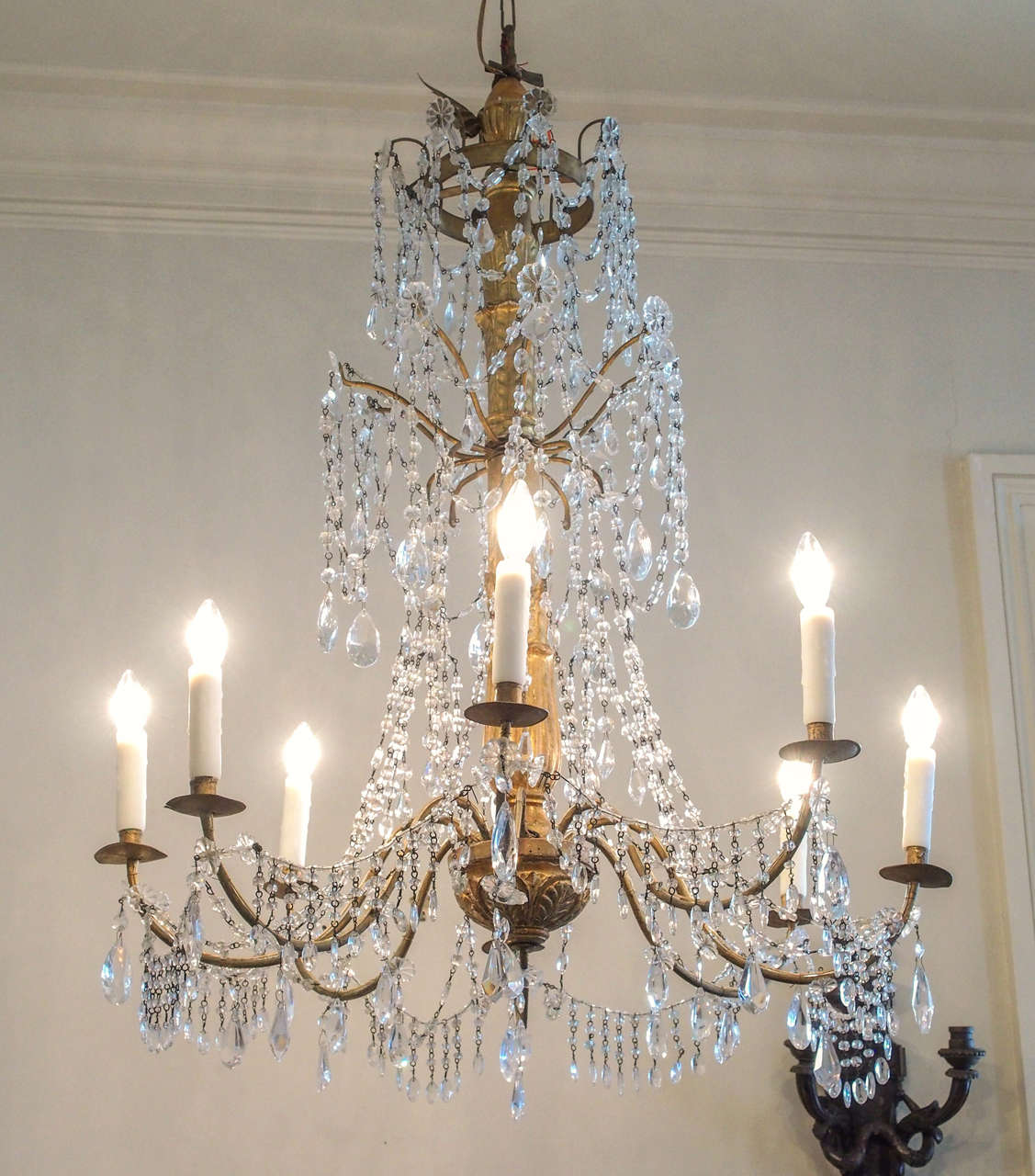 An elegant rendition of the Genovese chandelier, heavily festooned with swags of petite crystals, in three tiers, the bottom tier supporting the electrified arms. The center support of gilded wood ornamented with elongated leaves.
