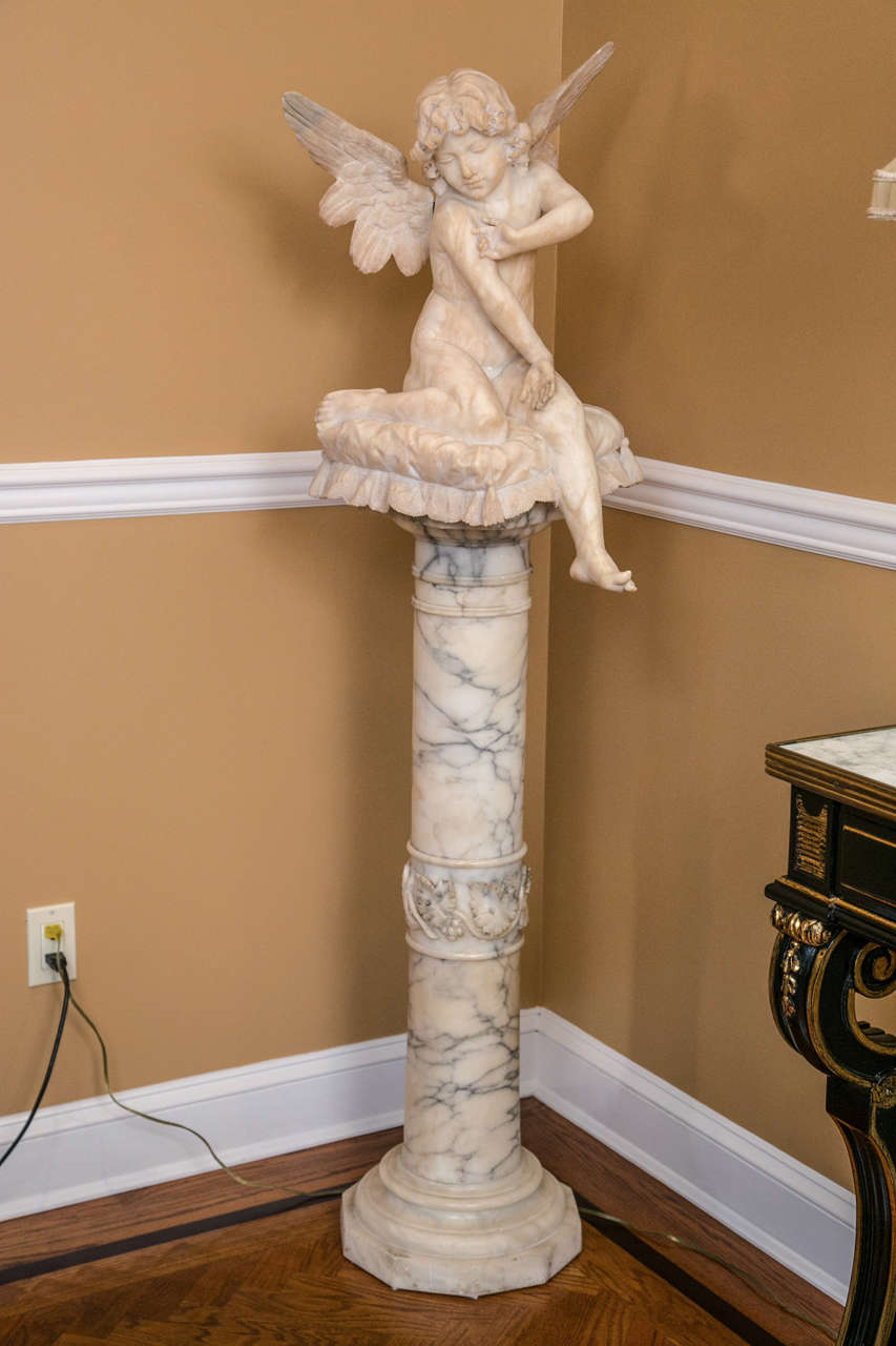 An alabaster figure on an alabaster pedestal. Simply stunning alabaster figure of a winged angel sitting on a pillow staring at her pinkie finger. The carved and twisted alabaster pedestal supporting this finely chiseled figure. The pillow custom
