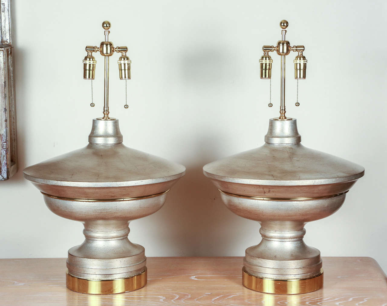 Pair of large table lamps in the form of flattened urns.  They are finished in silver leaf, with a thin brown glaze for the effect of a patina. There  are brass appointments and bases. The lamps have been newly rewired with double clusters