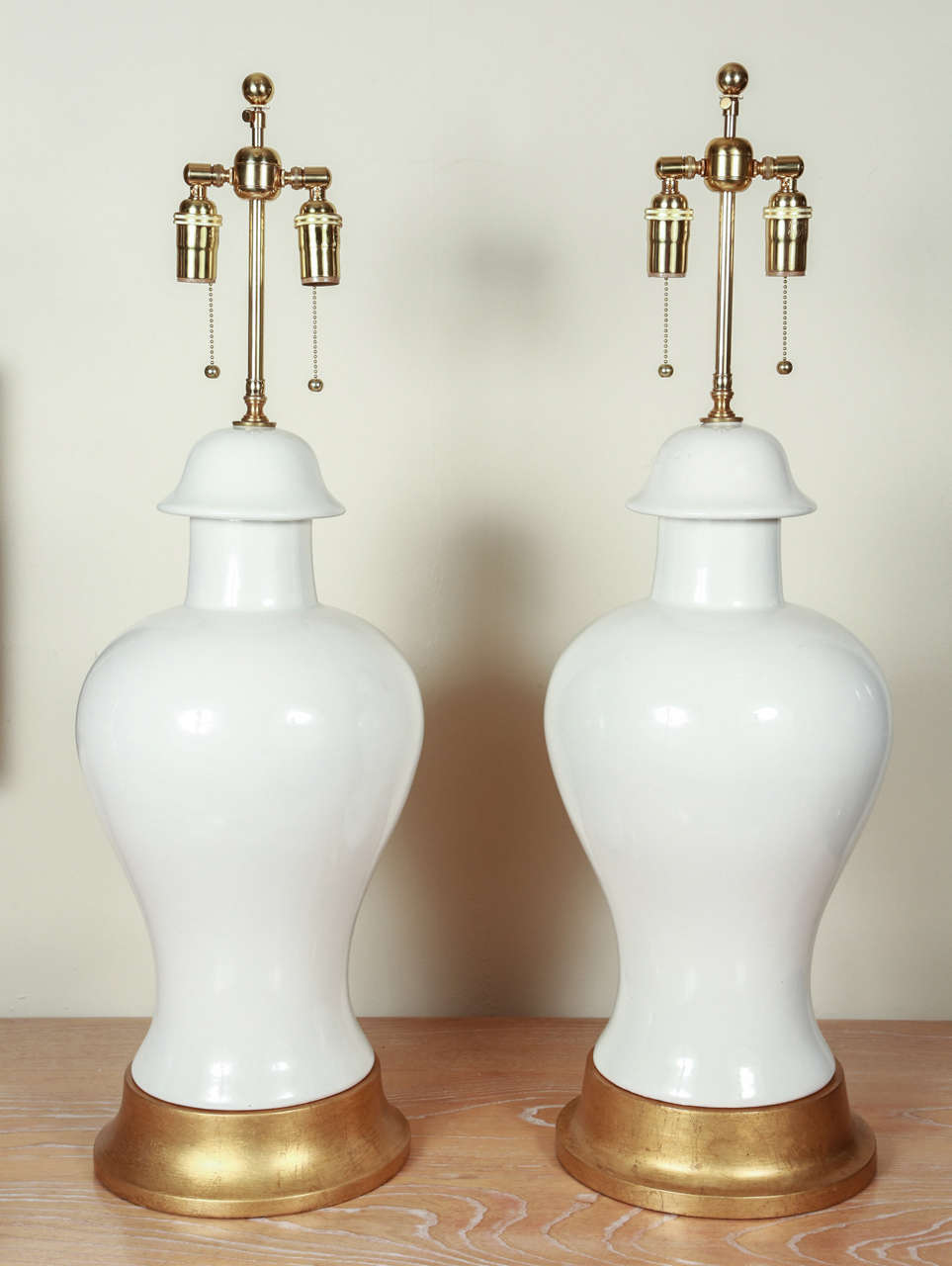 Pair of very large ginger jar style ceramic lamps.  The glaze is glossy white, with no crackling.   They are up on gilded wooden bases, and are newly rewired with brass double clusters.