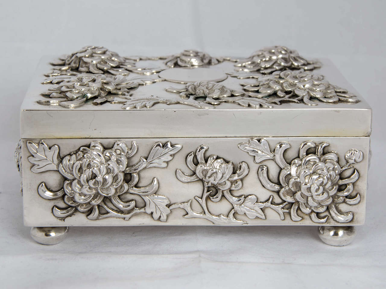 A Chinese export silver box with applied pronounced chrysanthemum decoration to the hinged lid and all four sides. The box was made circa 1890 by the firm of Hung Chong who had shops in Shanghai and Canton.
The box stands on four bun feet and