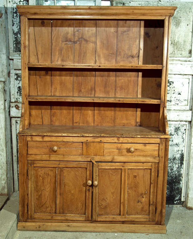 HAVING A MOULDED CORNICE- SHAPED SIDES -PINE WORK DECK ABOVE 2 MOULDED DRAWERS--2 PANELED DOORS BELOW. INTERIOR SHELVES FLOT BAE. NOTE: THIS PIECE APPEARS TO HAVE BEEN MADE BY A CARPENTER, NOT A CABINET MAKER- MADE IN GALWAY IN 1860